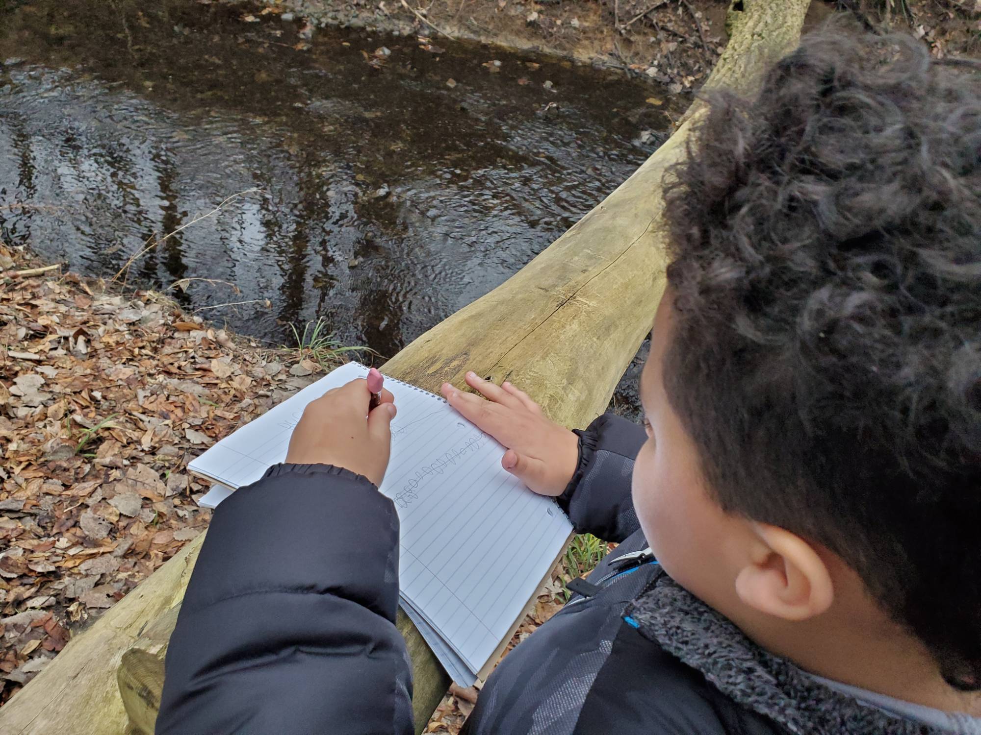 Student writing on notepad and looking at water from a bridge